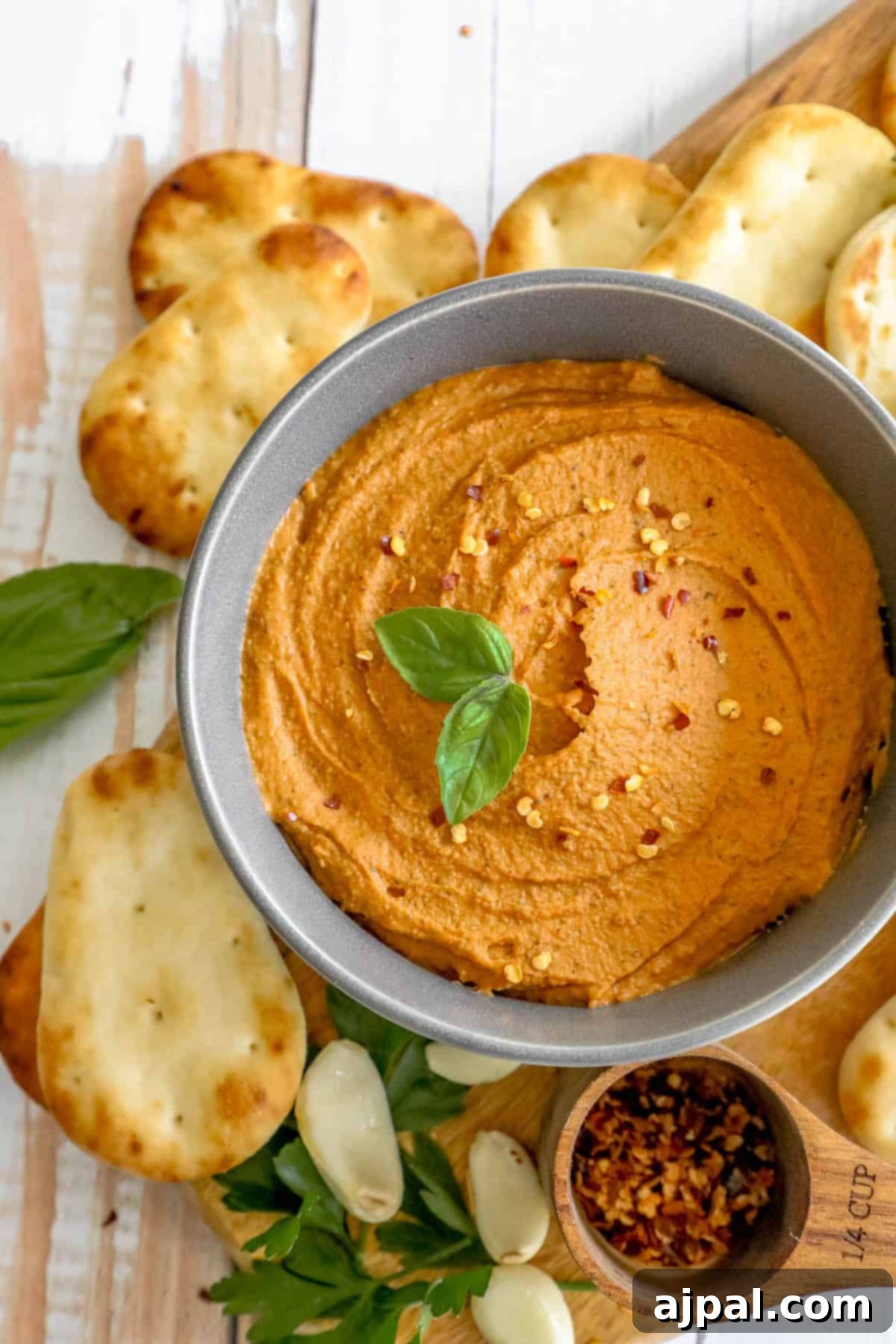 A rustic wooden cutting board holds a bowl of smooth pizza hummus, accompanied by an assortment of crunchy crackers, ready for dipping.