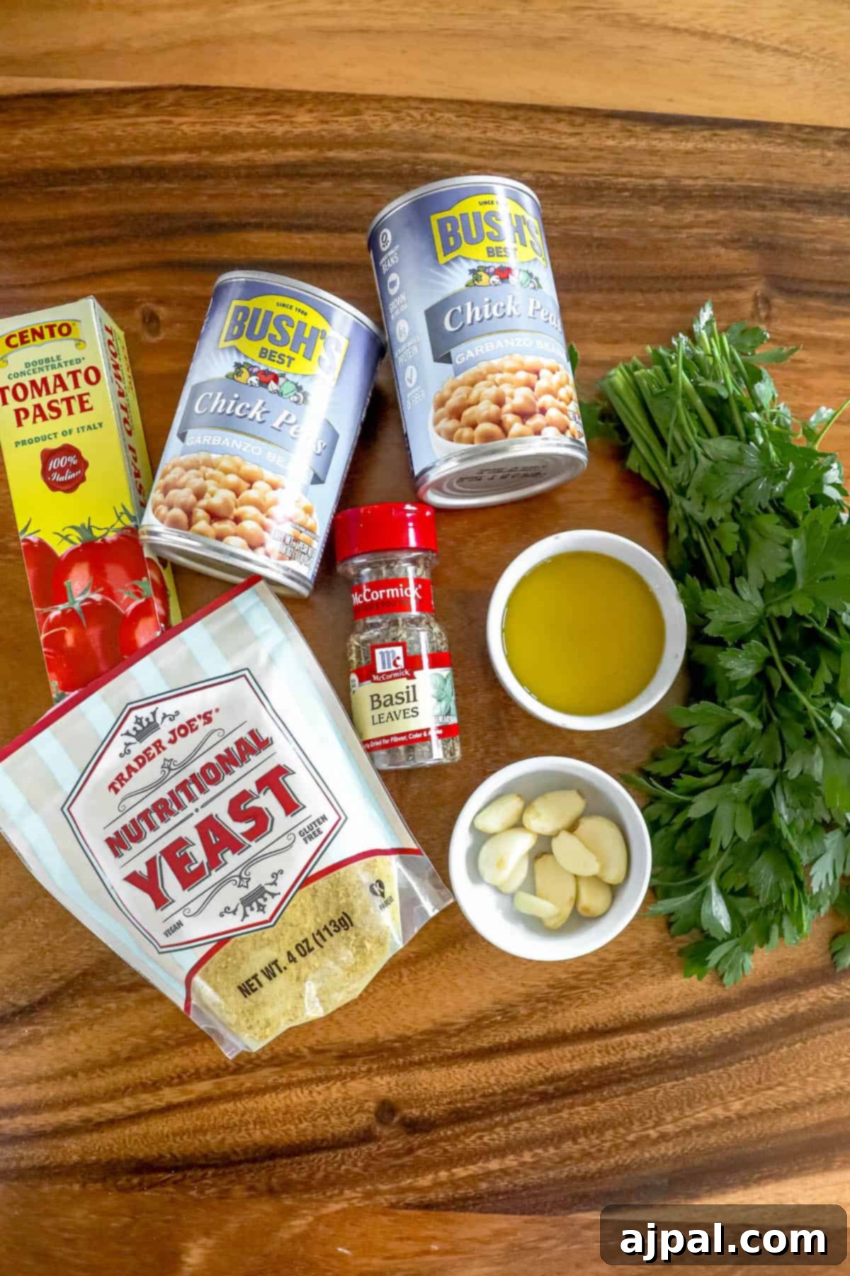 A collection of fresh ingredients for a flavorful dip, including whole tomatoes, garlic cloves, fresh basil leaves, and a bottle of olive oil, artfully arranged on a wooden surface.