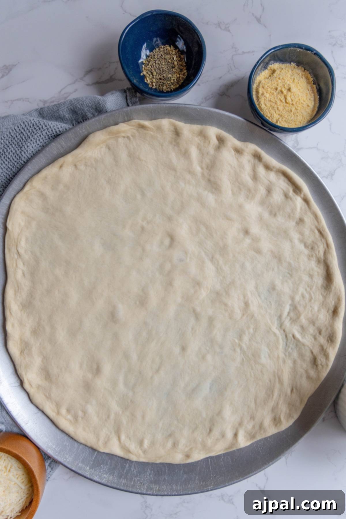 Smooth, easy homemade pizza dough stretched and ready on a light marble countertop.