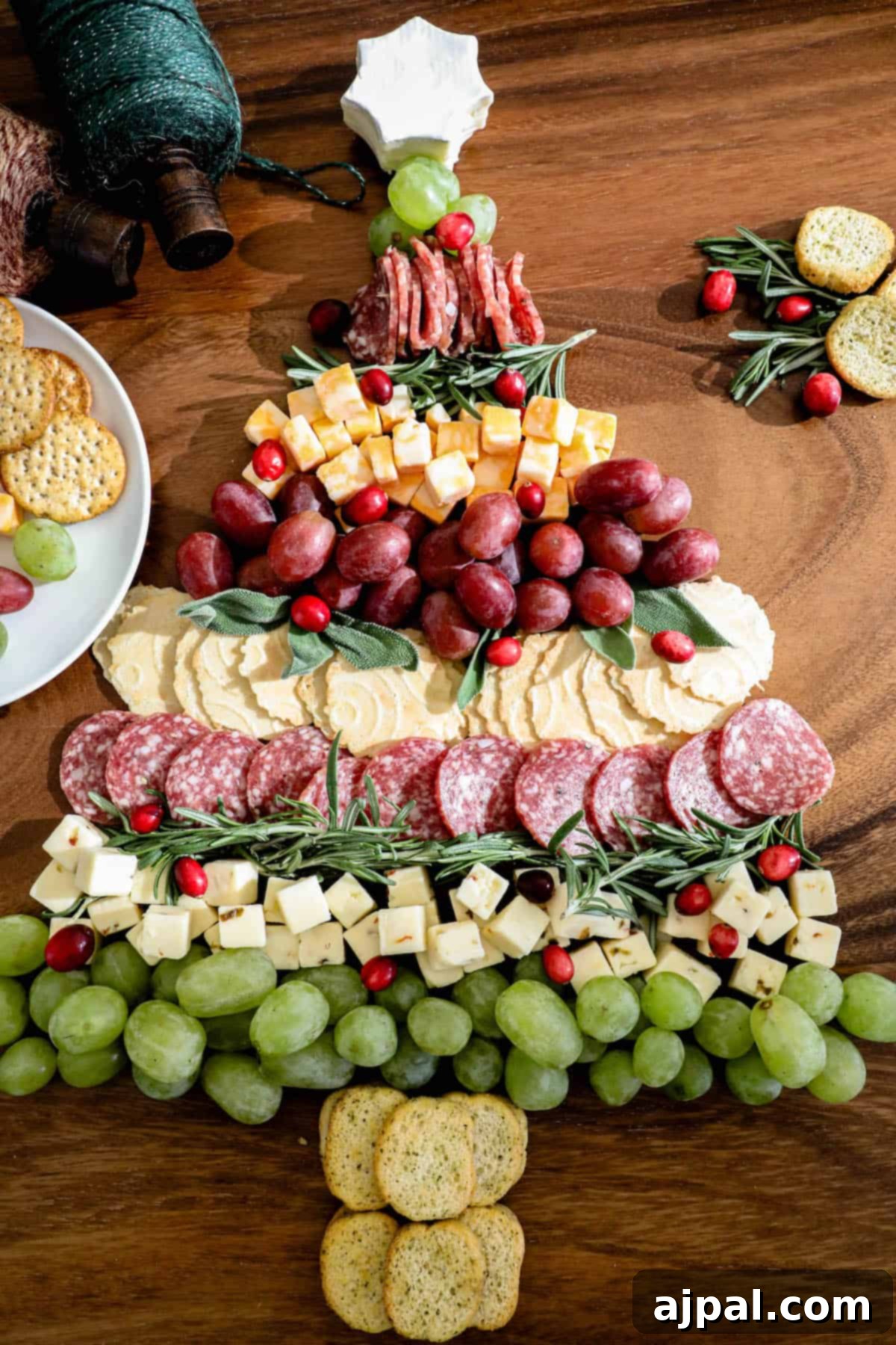 A festive Christmas cheese board adorned with a delightful assortment of crackers, grapes, and a cheese Christmas tree centerpiece.