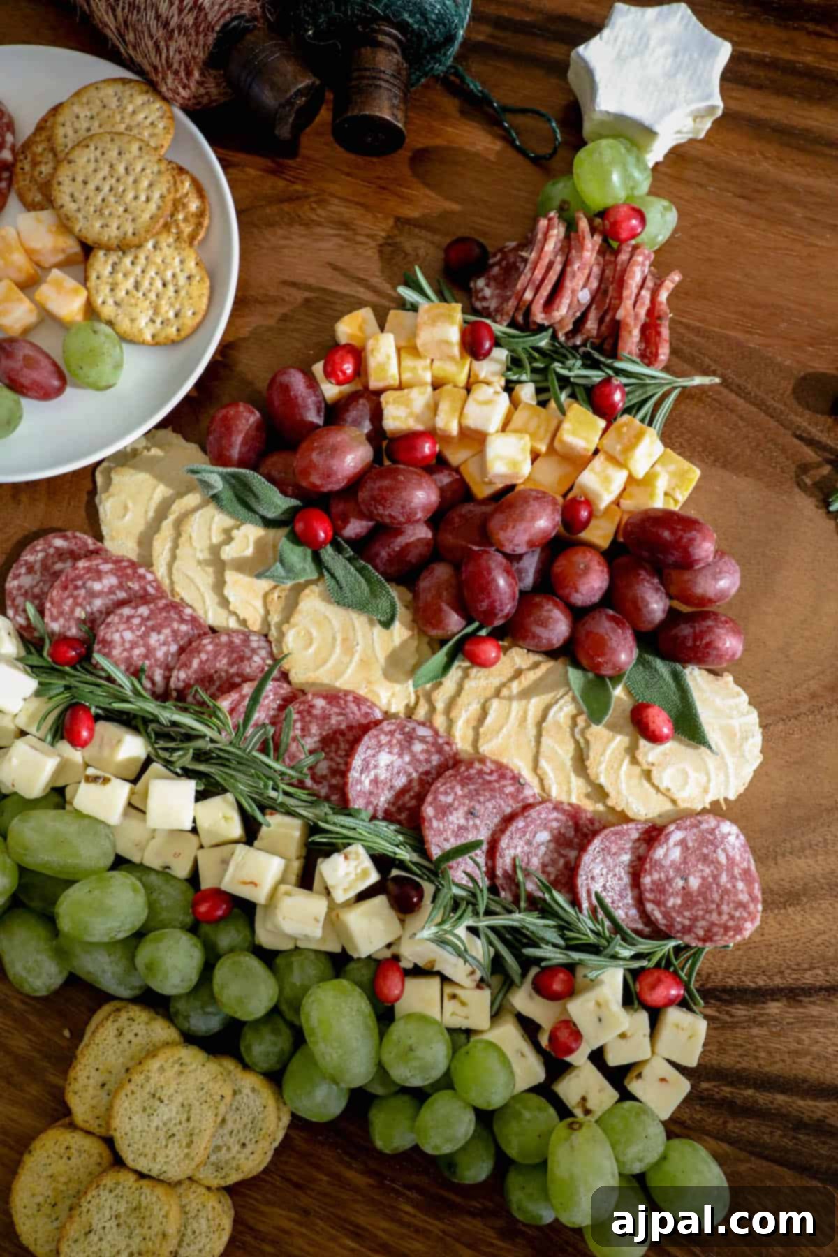 Holiday Cheese Delights 4 A beautifully arranged Christmas cheese board, in the shape of a Christmas tree, with various cheeses, crackers, grapes, and herbs.