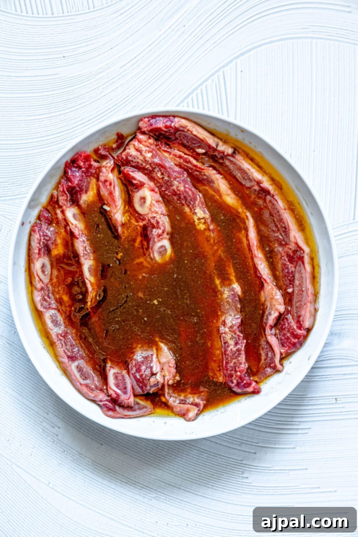 Korean BBQ Galbi Flanken Ribs 4 Flanken ribs luxuriously bathing in a rich Korean BBQ marinade within a glass dish, absorbing the irresistible flavors.