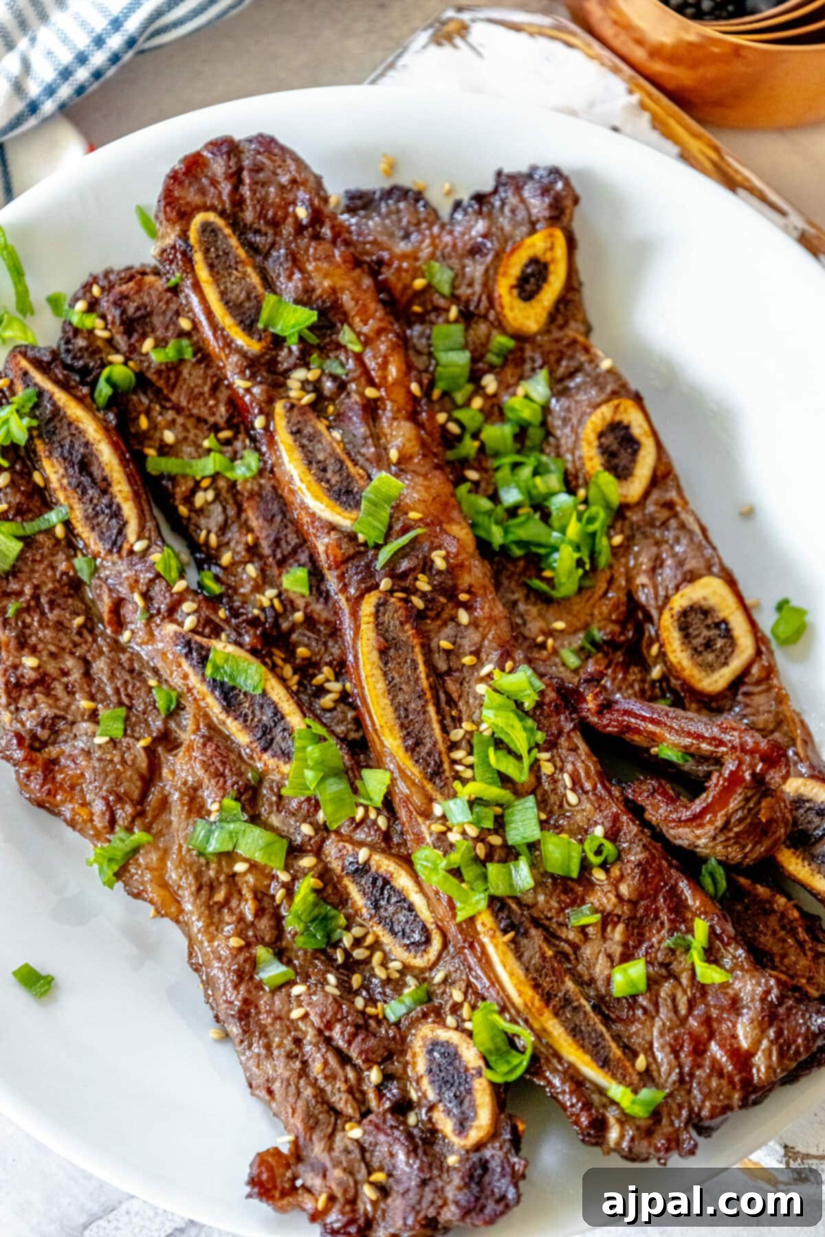 Korean BBQ Galbi Flanken Ribs 6 A vibrant display of Korean beef flanken ribs on a white plate, meticulously garnished with toasted sesame seeds and freshly diced green onions.