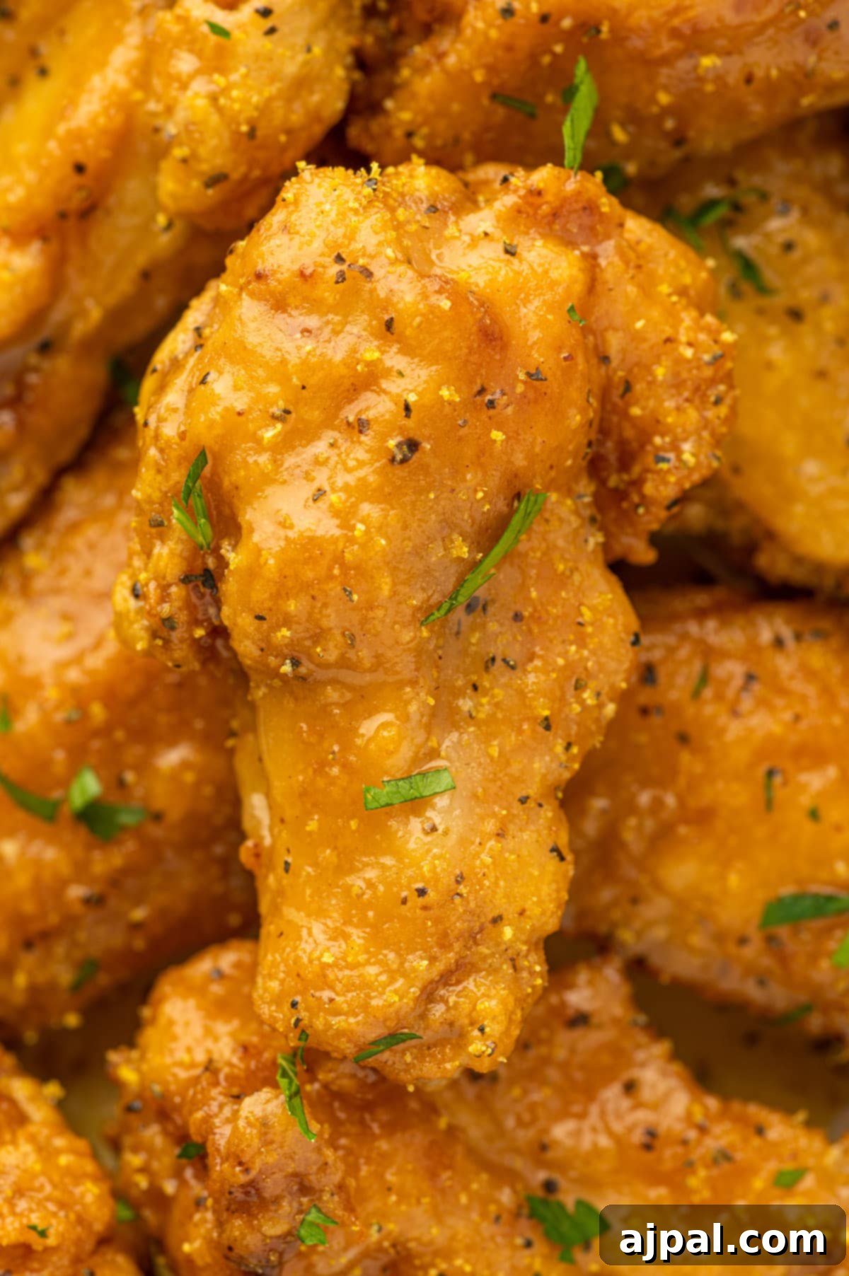A close up of golden-brown lemon pepper chicken wings on a plate, garnished with fresh parsley.