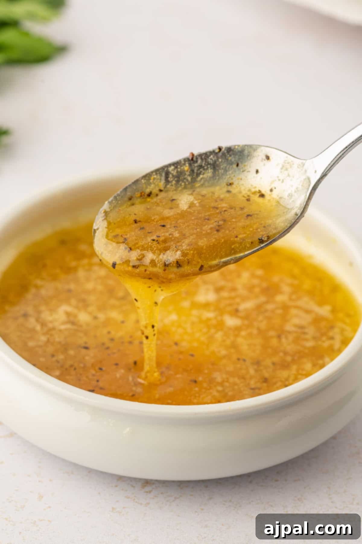 A spoon pouring luscious lemon butter sauce over freshly fried chicken wings in a bowl.