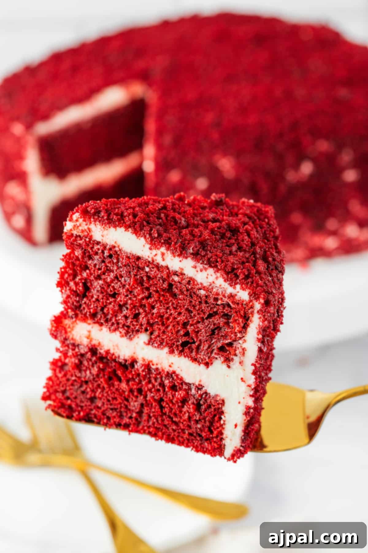 A delicious slice of red velvet cake, showcasing its vibrant layers and creamy frosting, elegantly placed on a white plate.