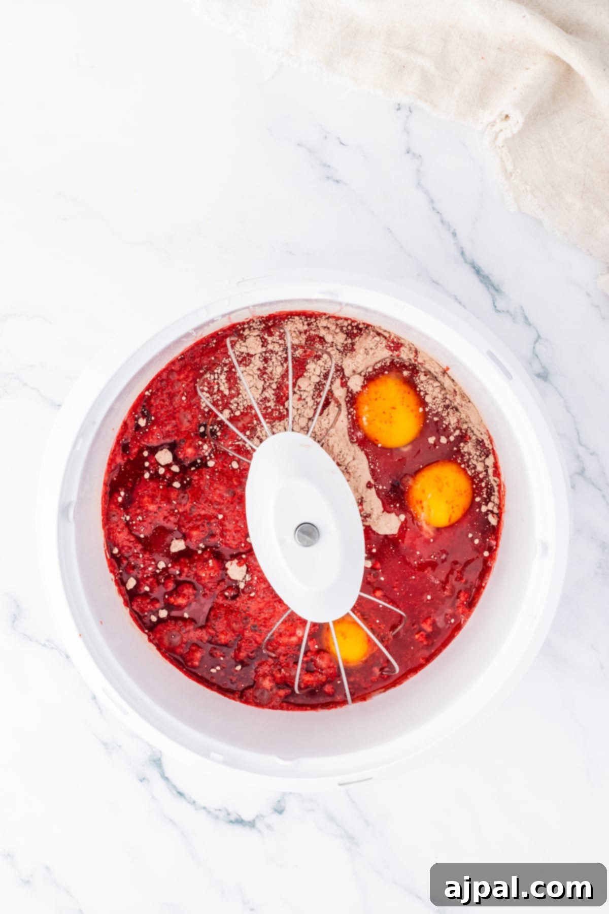 A white bowl holds a vibrant red liquid, resembling the rich batter of a Red Velvet Cake, ready for baking.