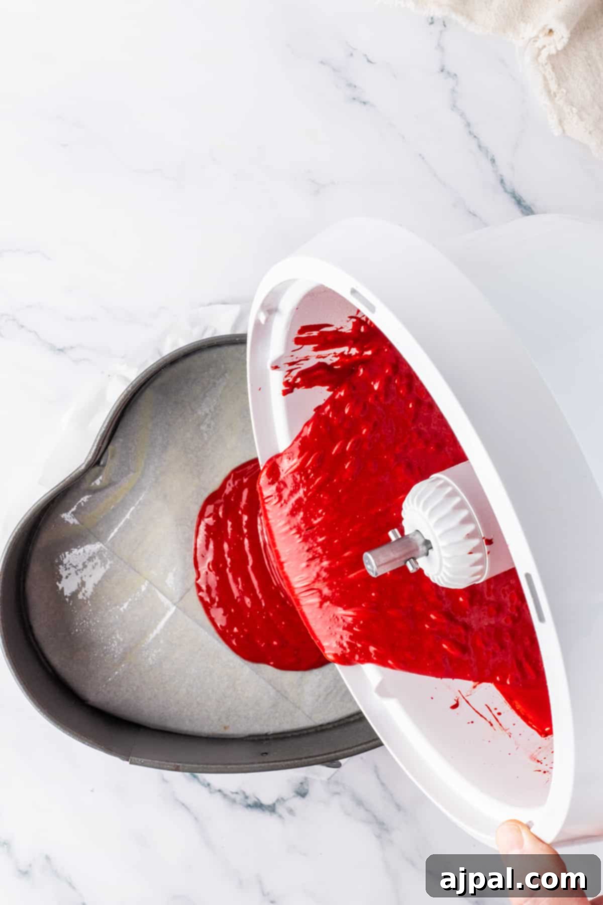 A person expertly pours luscious red icing over a freshly baked Red Velvet Cake, creating a smooth, glossy finish.