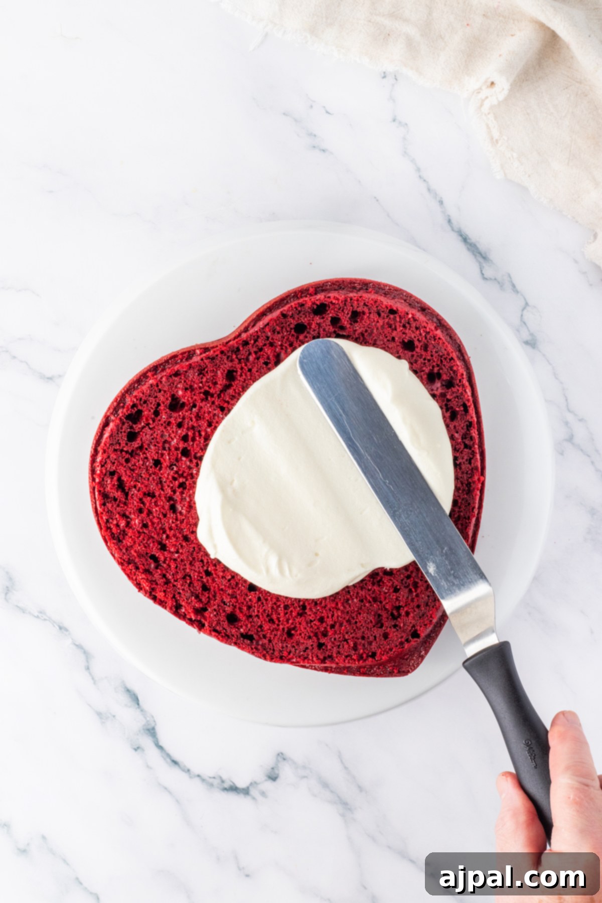 A hand gently cuts into a rich red velvet cake with a knife, promising a delightful slice.
