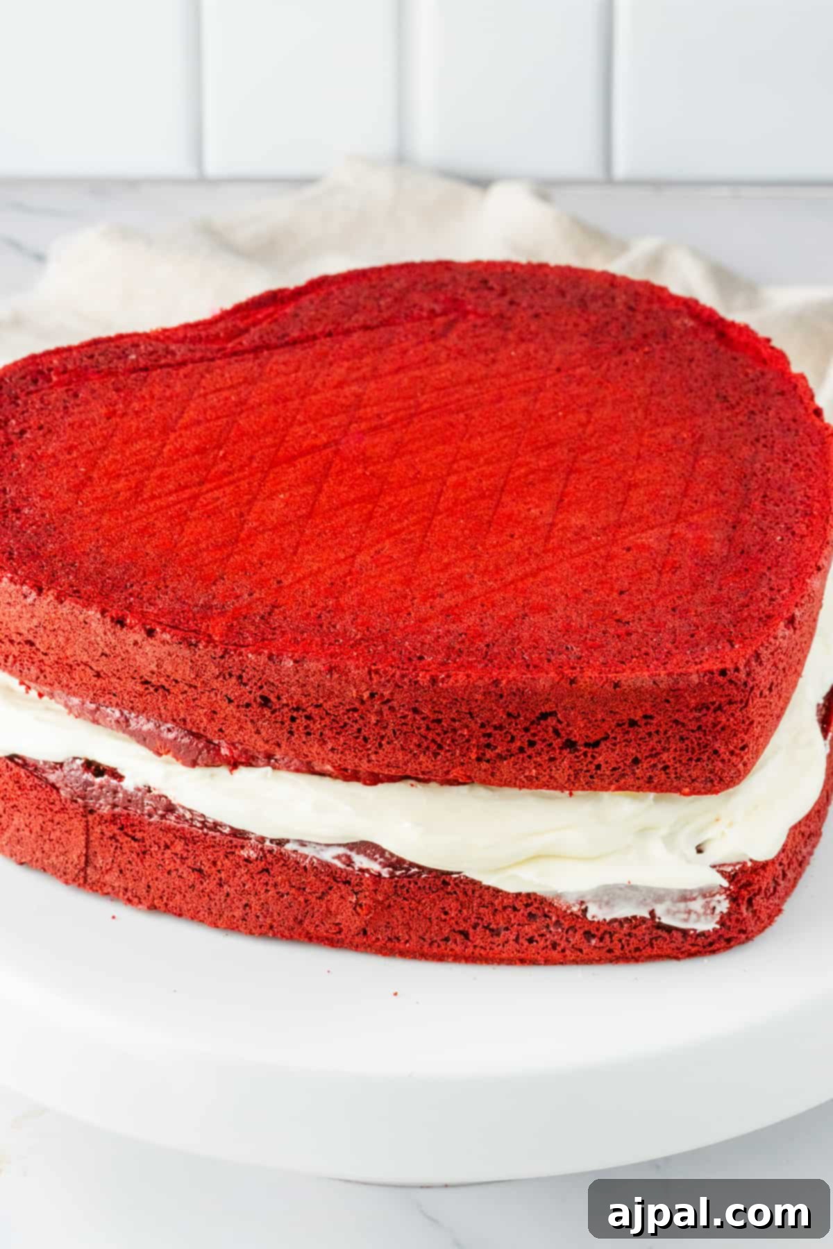 A beautifully crafted heart-shaped red velvet cake sits invitingly on a white plate, adorned with creamy frosting.