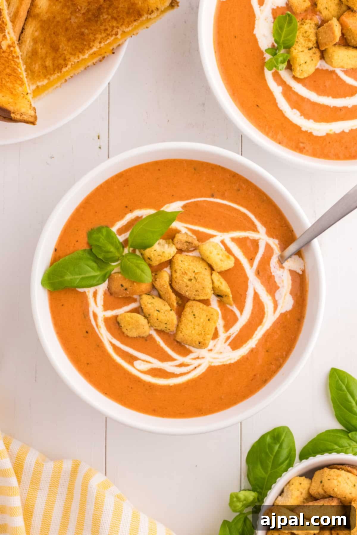 Two bowls of creamy roasted red pepper and tomato soup, garnished with fresh basil and croutons.