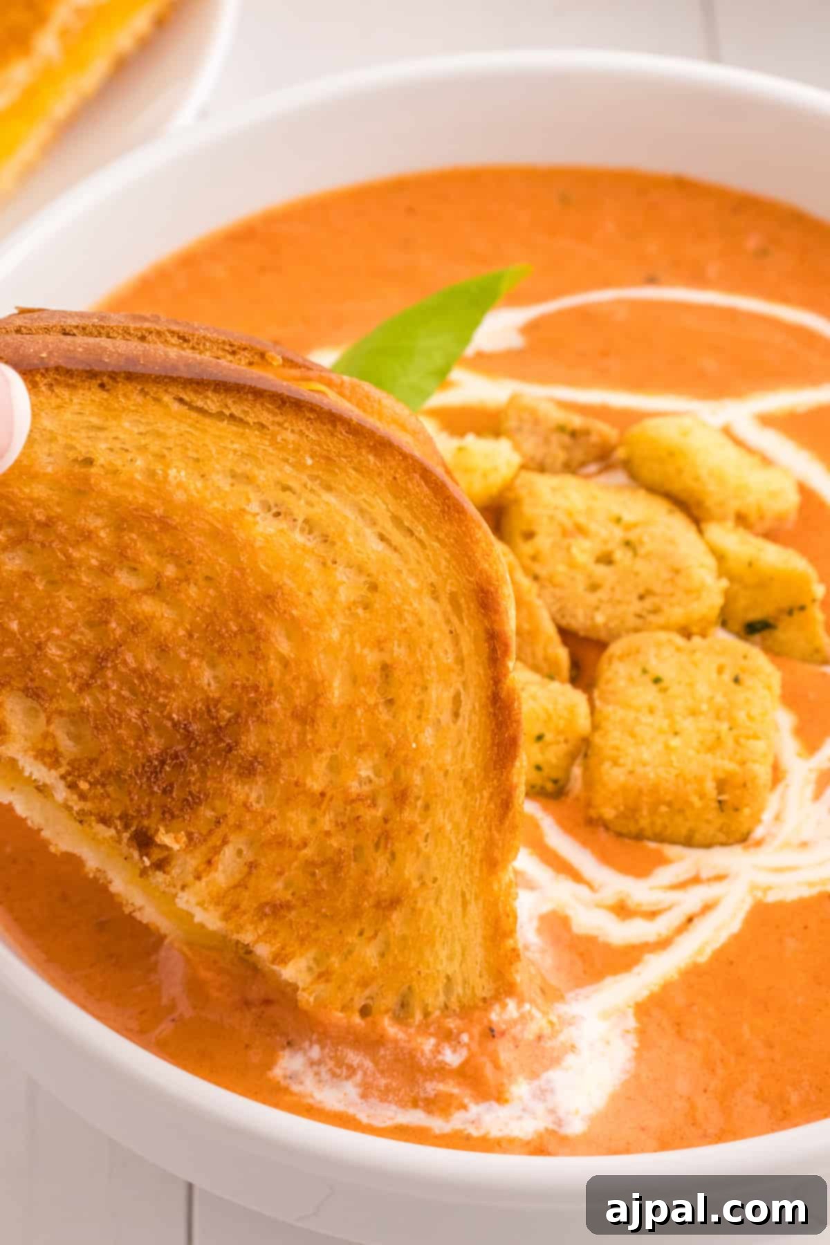A bowl of rich, creamy tomato soup topped with toasted croutons and a swirl of cream.