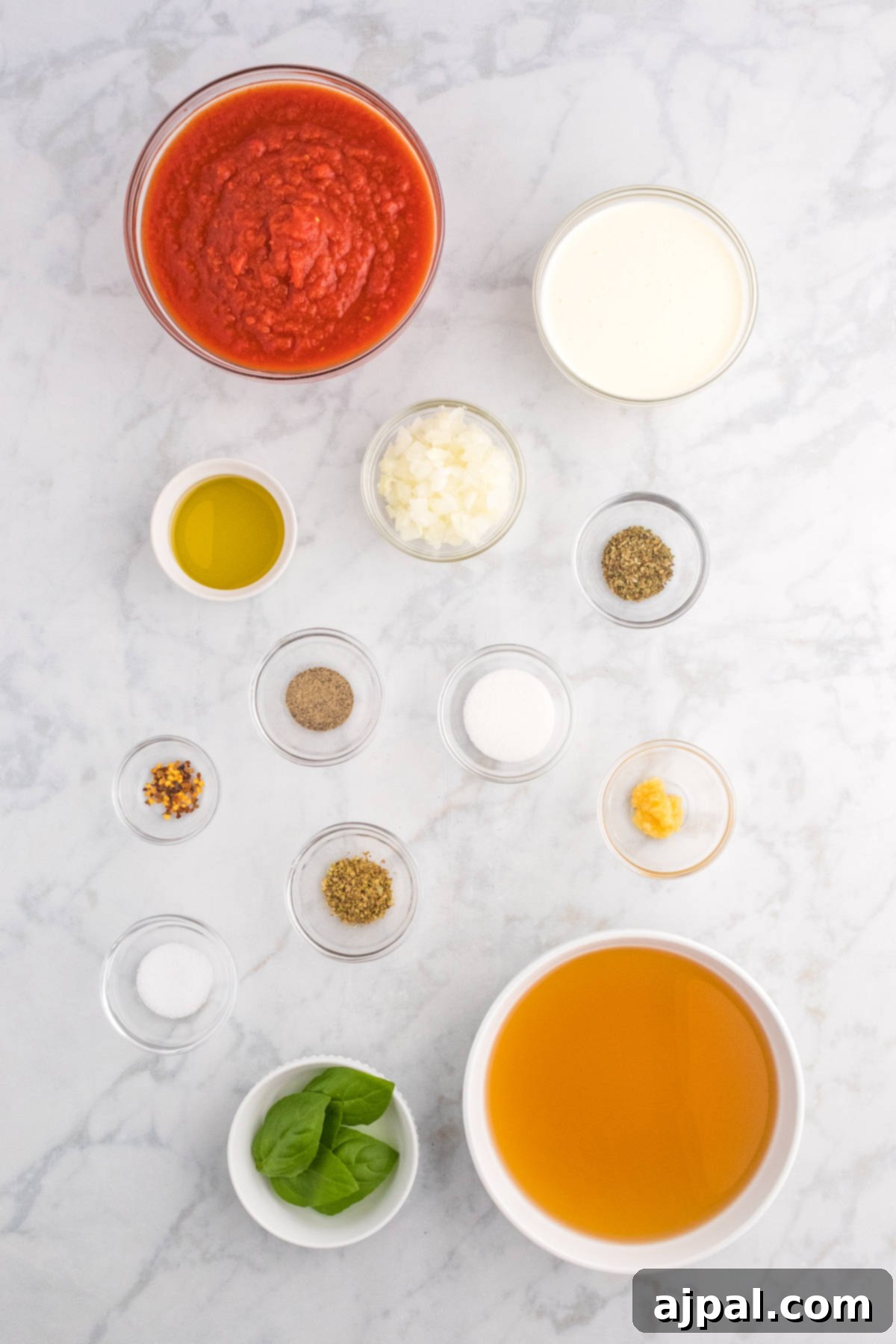 The vibrant ingredients for a red pepper tomato soup laid out on a marble countertop, including fresh bell peppers, ripe tomatoes, onions, and herbs.