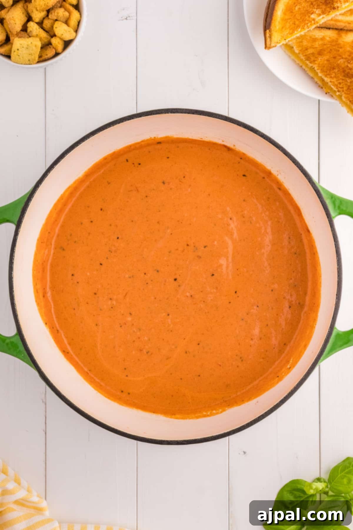 A comforting bowl of red pepper tomato soup, accompanied by crusty bread and golden croutons, perfect for a cozy meal.