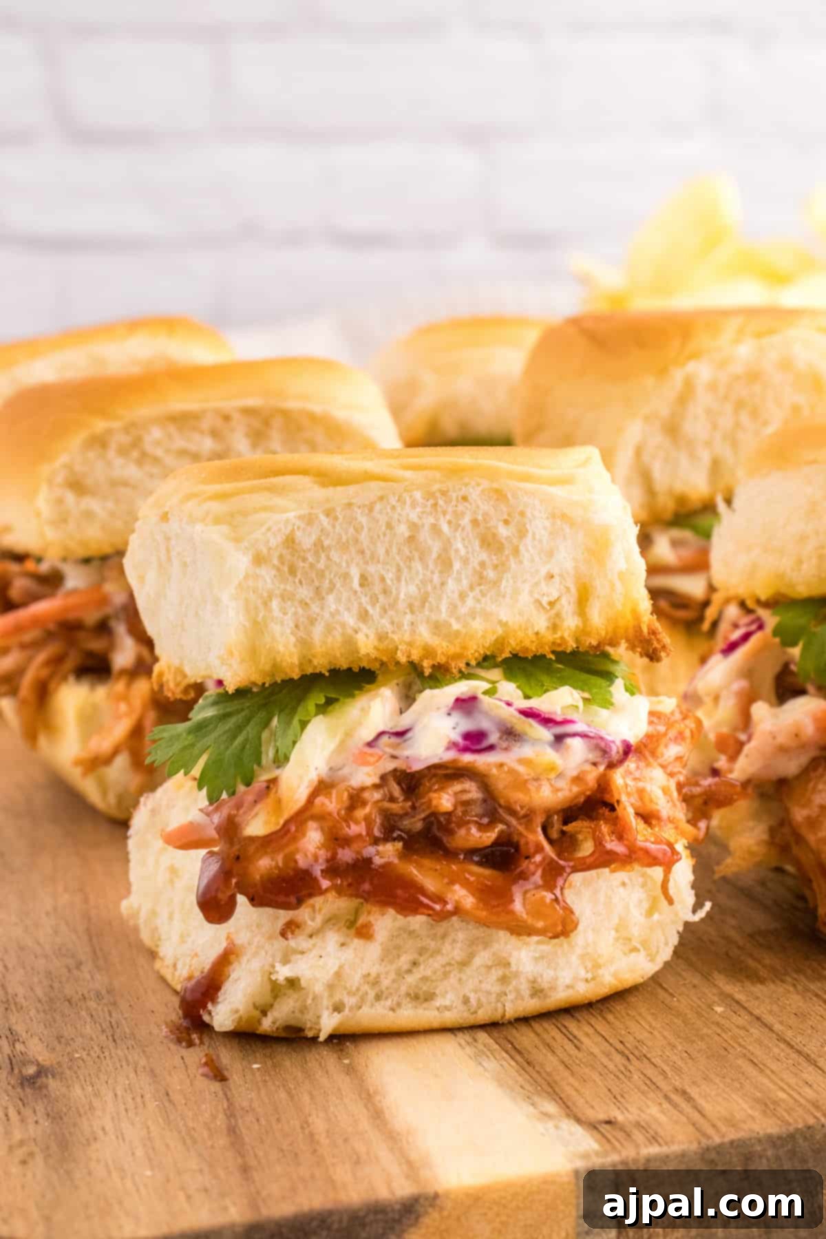 Smoky BBQ Chicken Minis 2 Close-up of BBQ pulled chicken sliders on a rustic wooden cutting board, garnished with fresh herbs.