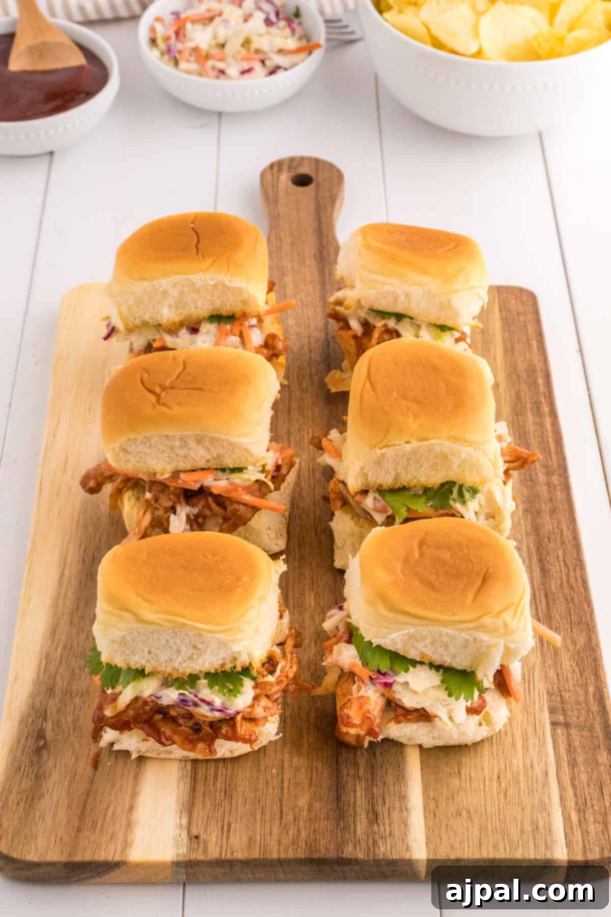 Smoky BBQ Chicken Minis 12 BBQ pulled chicken sliders served on a rustic wooden cutting board, with extra sauce and fresh herbs for garnish.