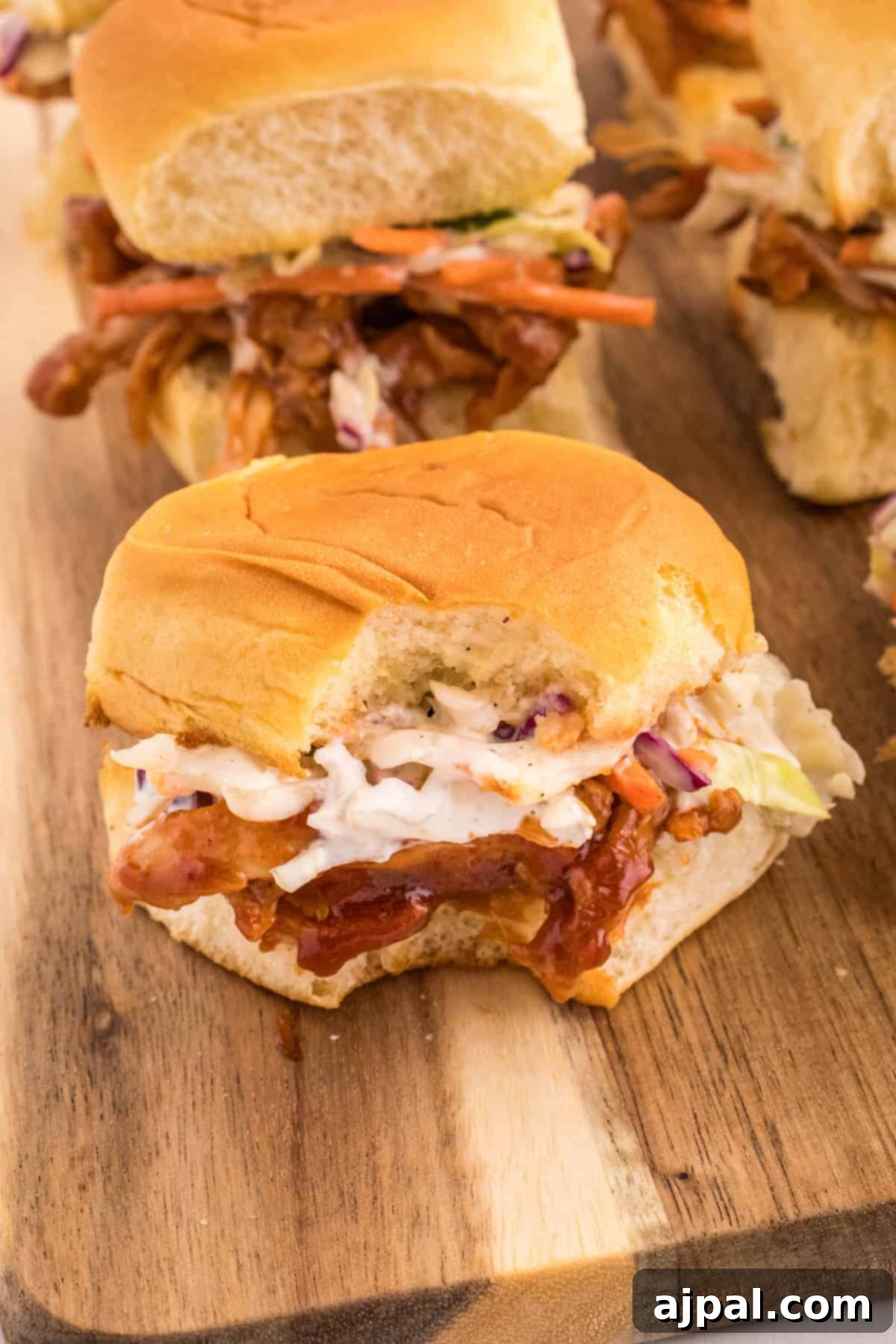 Smoky BBQ Chicken Minis 3 A serving of BBQ pulled chicken sliders arranged appealingly on a wooden cutting board.
