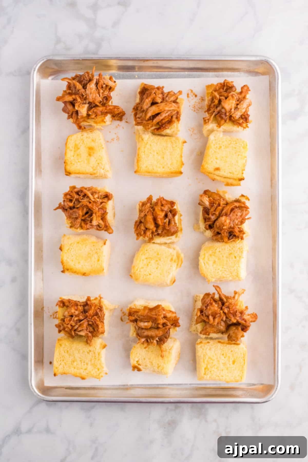 Smoky BBQ Chicken Minis 7 BBQ pulled chicken sliders arranged on a baking sheet, ready for the oven or serving.