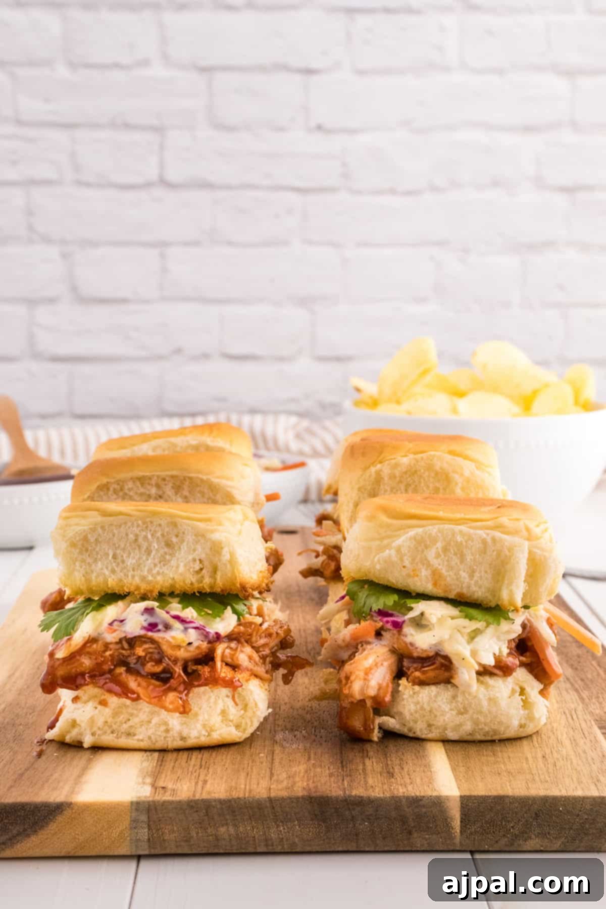 Smoky BBQ Chicken Minis 10 A vibrant close-up of BBQ pulled chicken sliders, topped with creamy coleslaw, served on a rustic wooden cutting board.