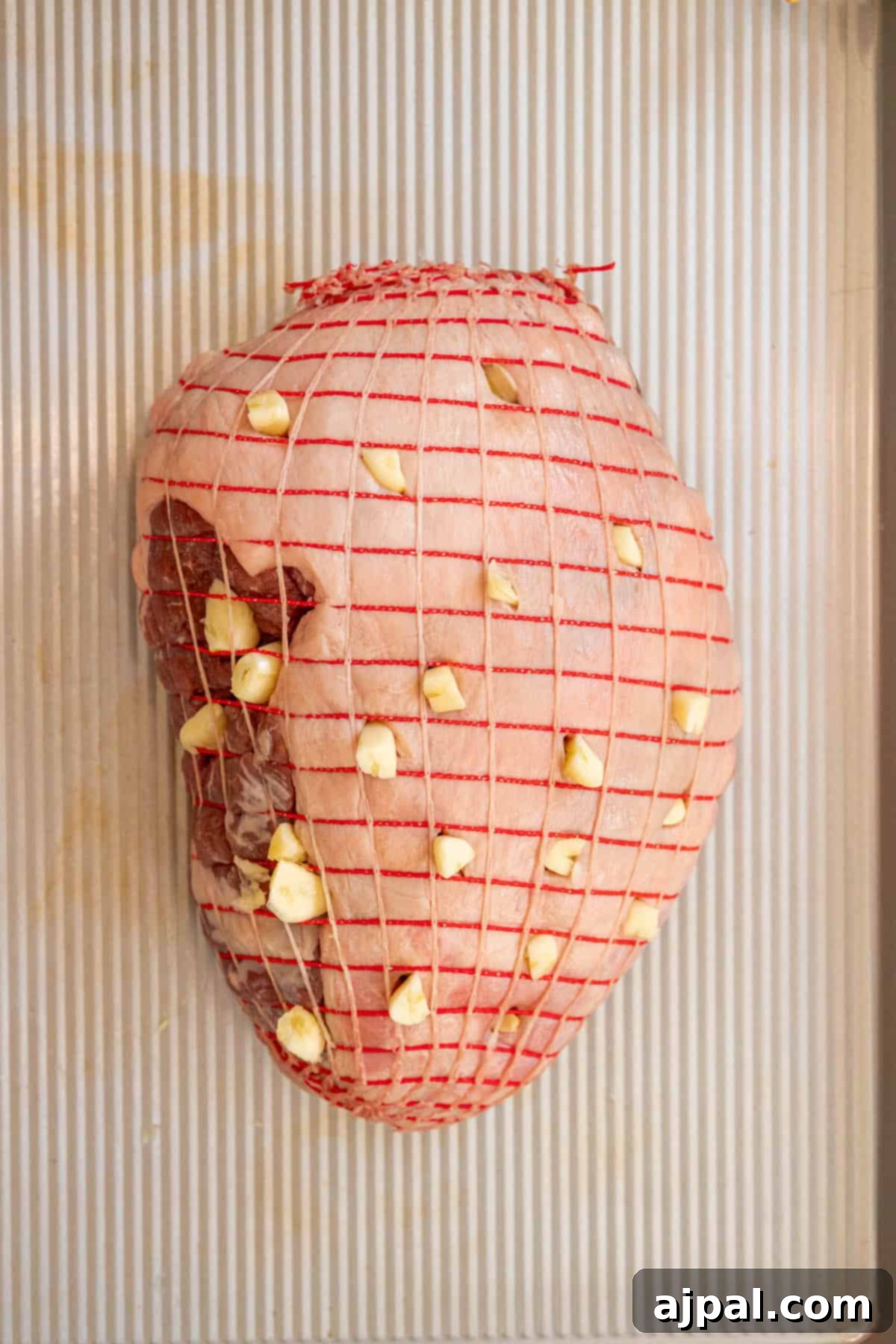 Succulent Reverse Seared Lamb Leg 4 A close-up of the scored leg of lamb, with garlic cloves tucked into the incisions, enhancing the flavor.
