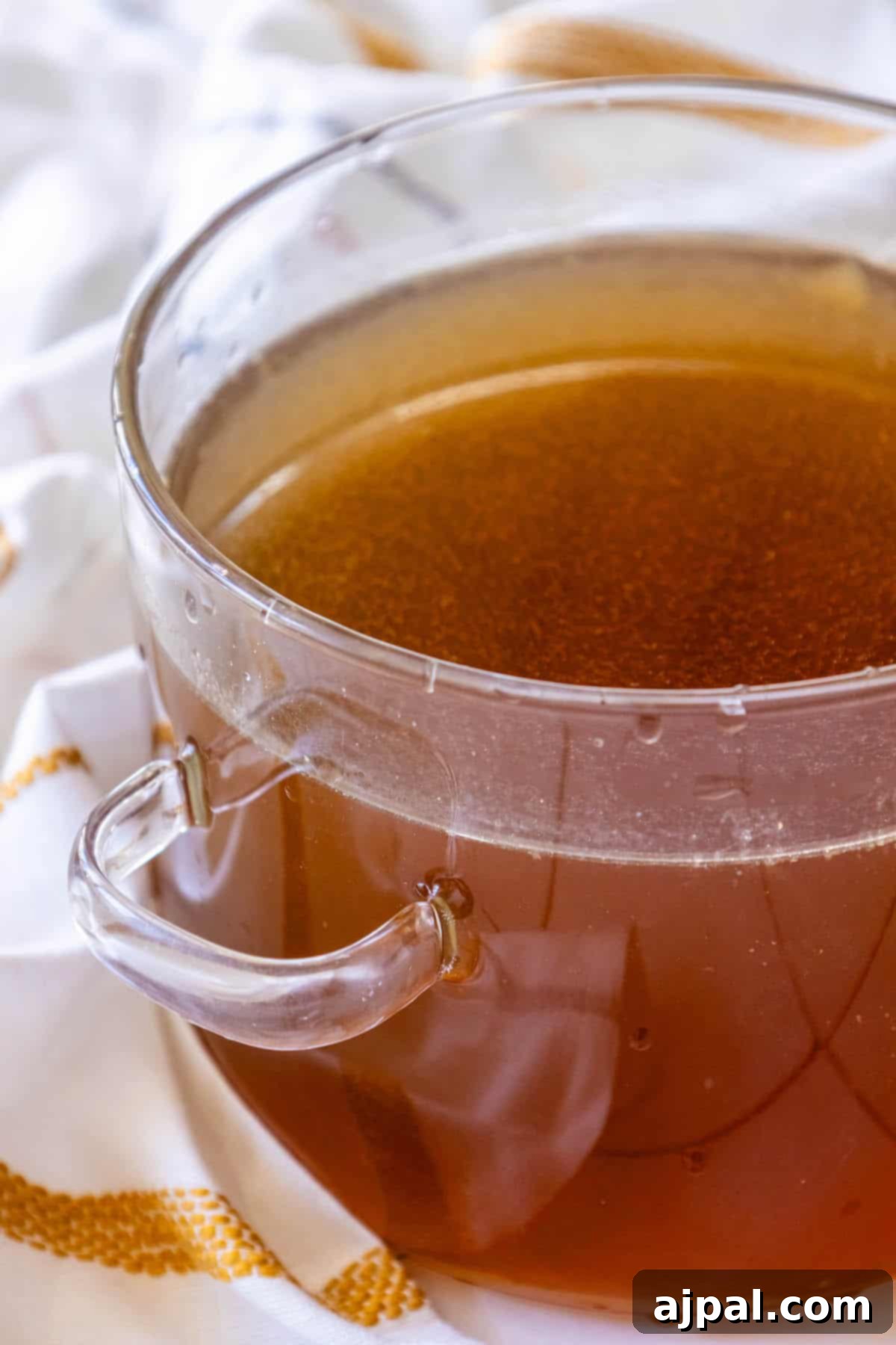 A glass bowl filled with golden homemade chicken stock, placed on a rustic wooden table, ready to be used in a delicious recipe.