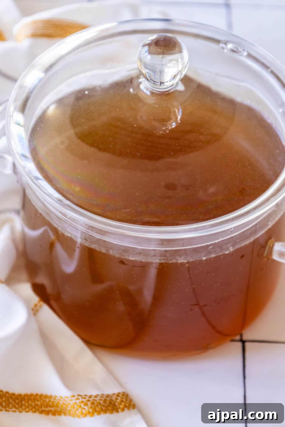 A large glass pot simmering on a stovetop, filled with the golden liquid of homemade chicken stock and various vegetables.
