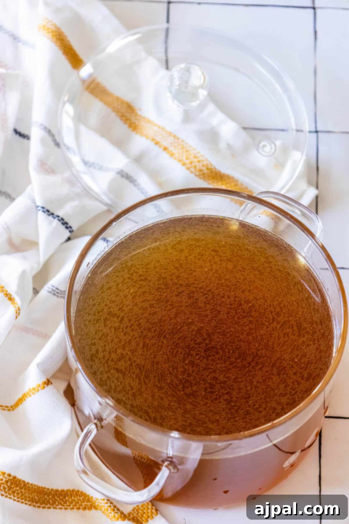 A rustic bowl of rich brown gravy, likely made with homemade chicken stock, resting on a textured white towel.