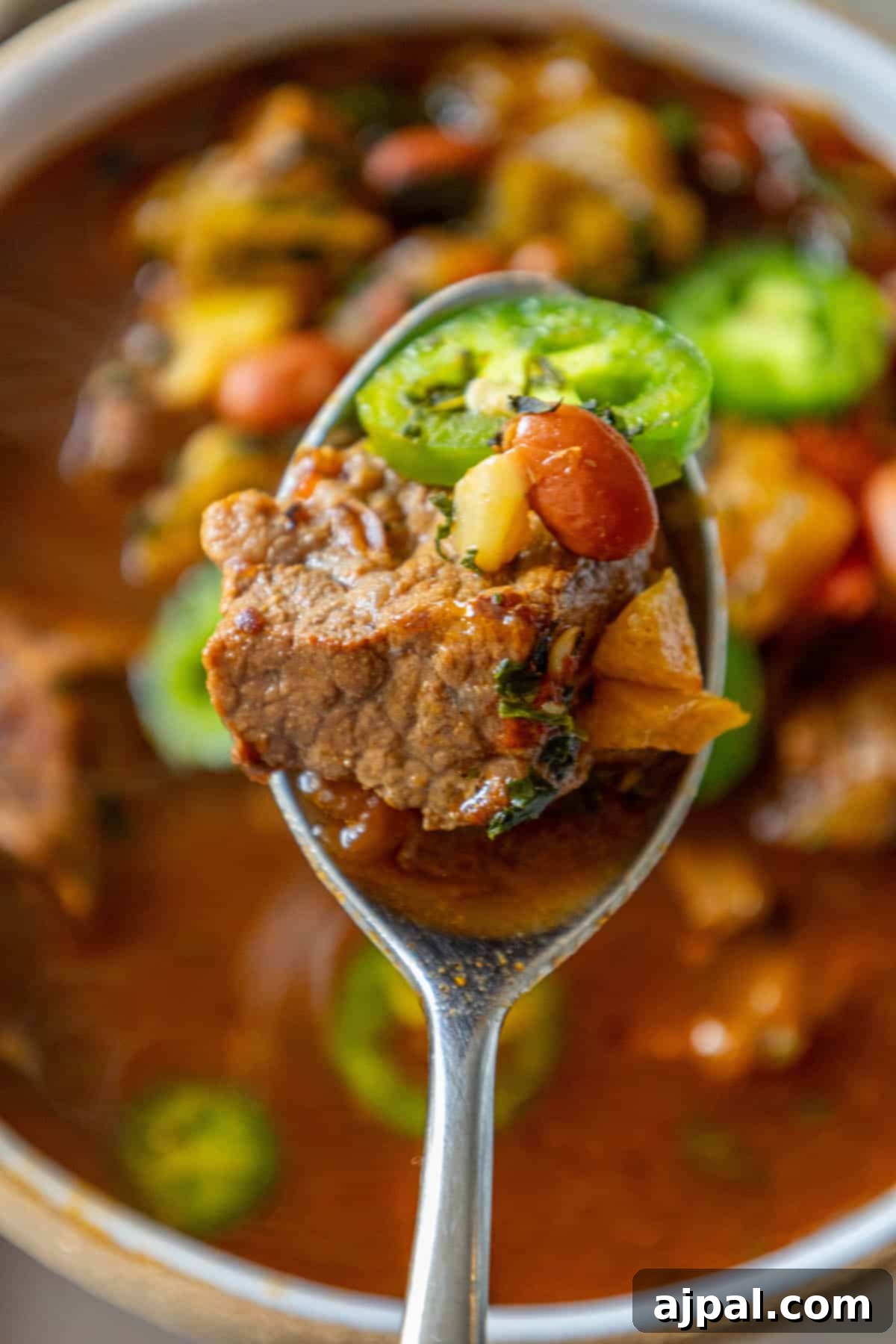 A spoonful of spicy beef soup with meat and beans lifted from a bowl, showing the hearty texture.
