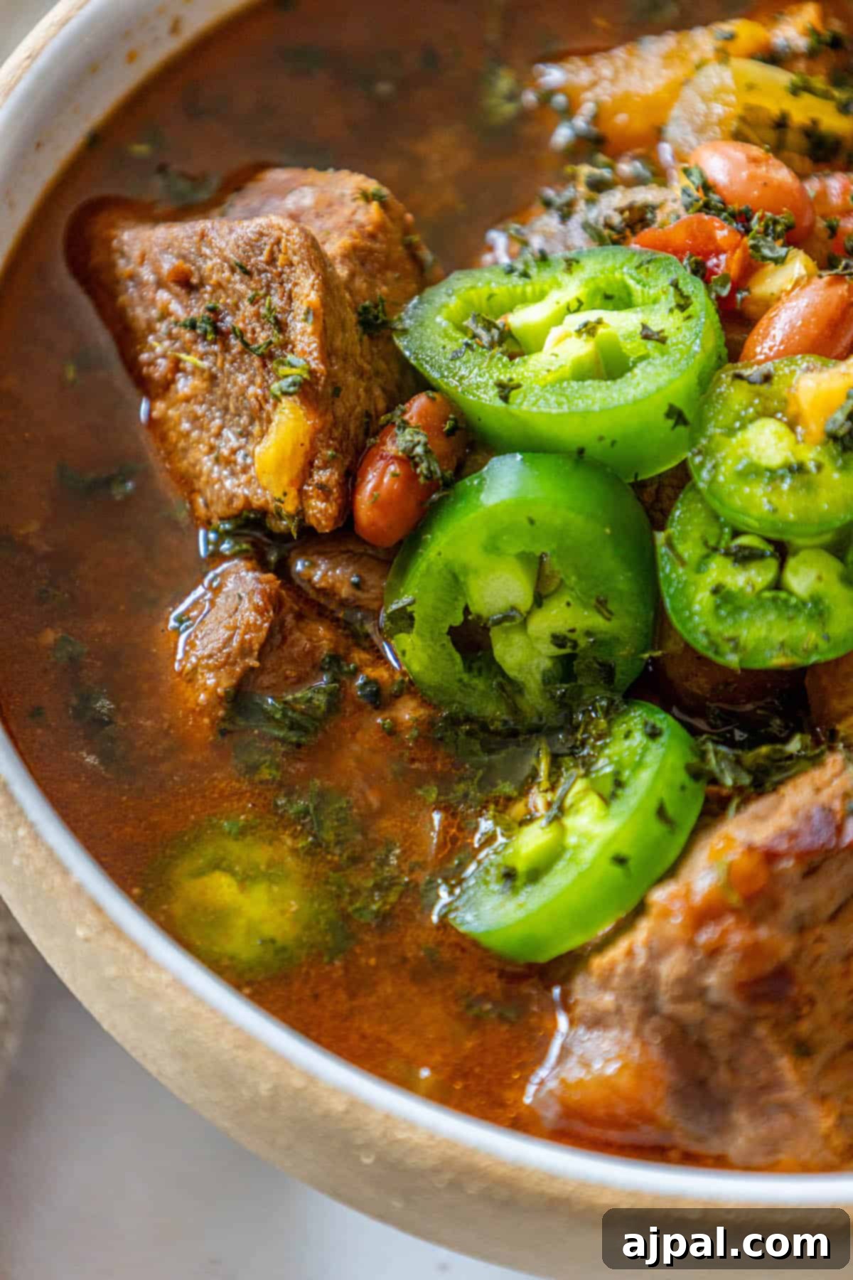 A deep bowl of stew, generously filled with succulent meat, various beans, and colorful peppers.