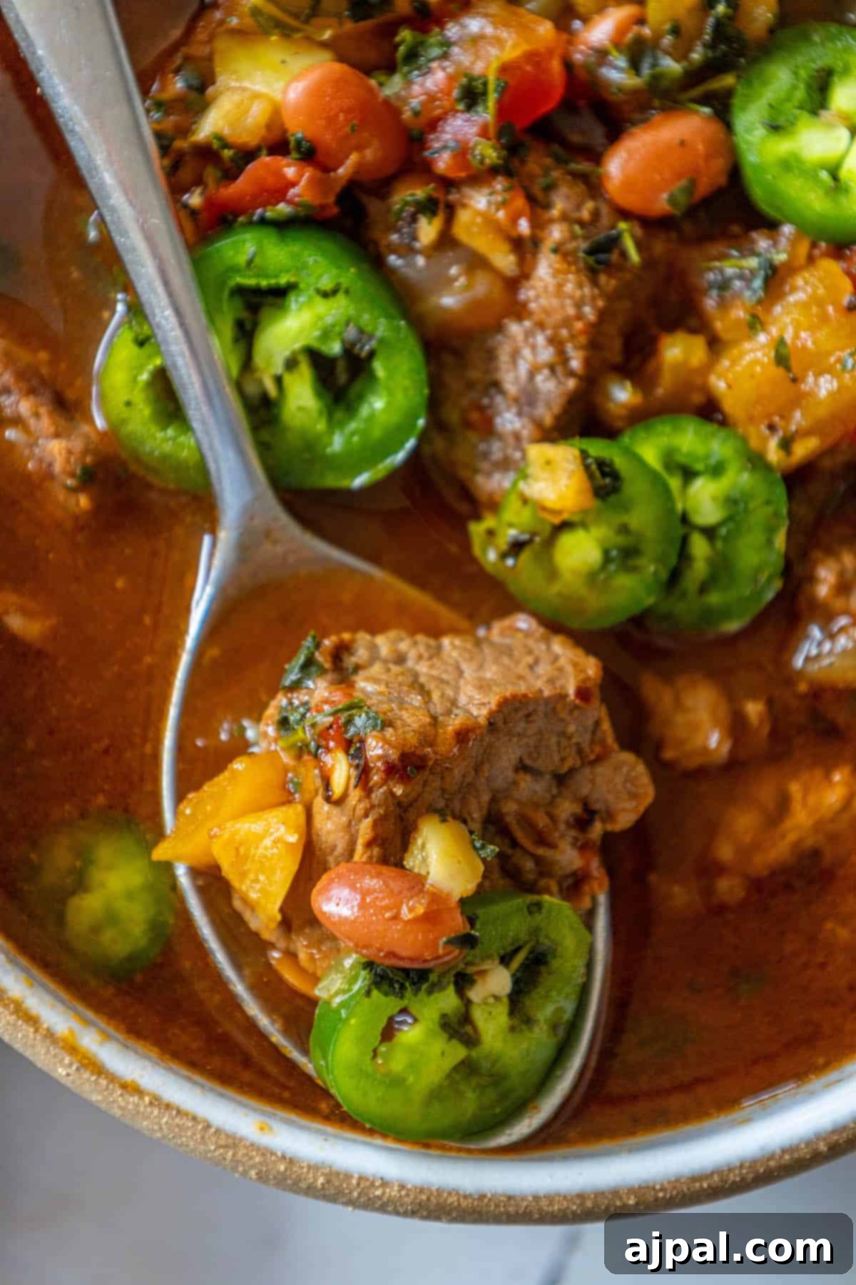 Spicy beef stew with succulent meat and vibrant jalapeño peppers, served in a rustic bowl.