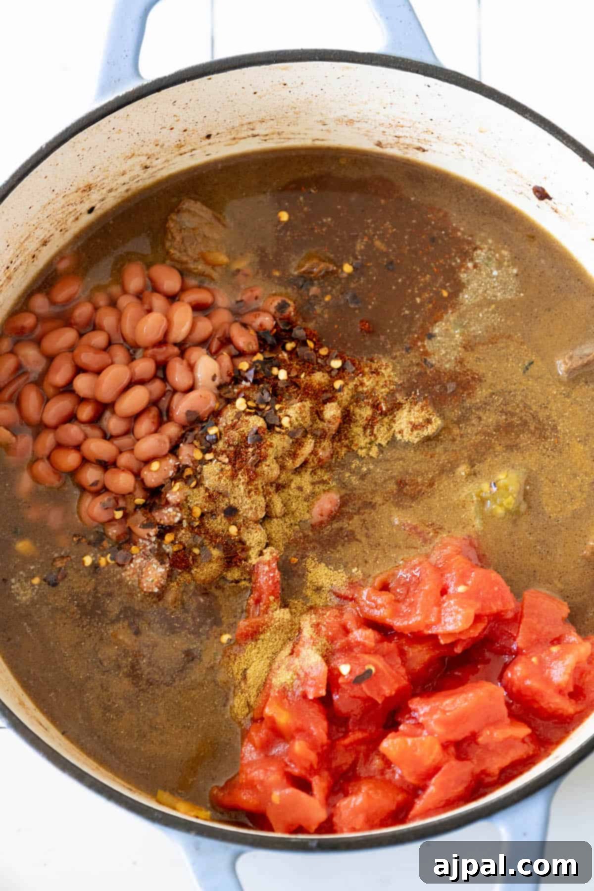 A close-up of a pot filled with spicy beef stew, showcasing a vibrant mix of jalapeños, beans, and diced tomatoes.