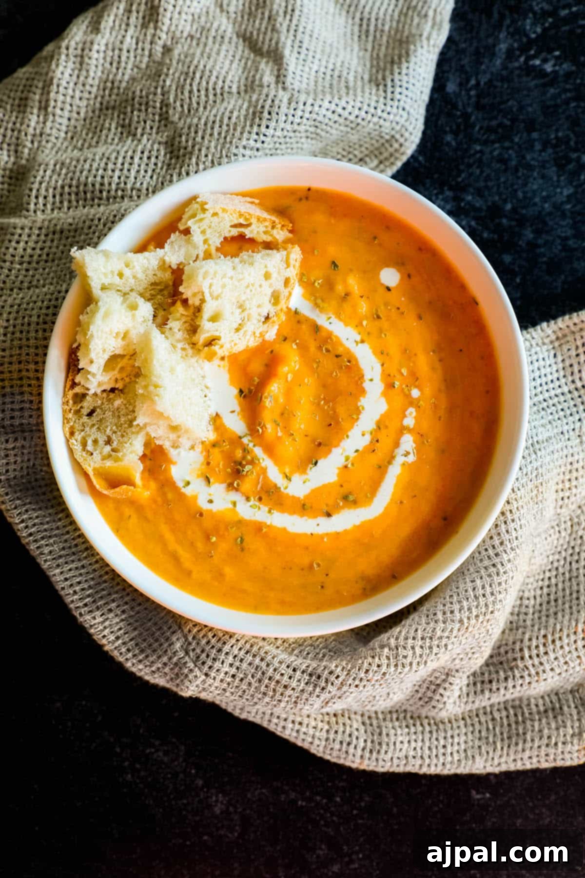 Hearty Roasted Tomato Soup 11 A rustic bowl of homemade Roasted Tomato Soup, artfully garnished with a slice of bread and fresh basil, ready to be enjoyed as a comforting meal.