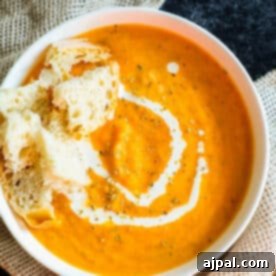 Hearty Roasted Tomato Soup 13 A bowl of vibrant orange creamy roasted tomato soup, topped with crunchy croutons and a drizzle of white cream, exuding warmth and inviting texture.