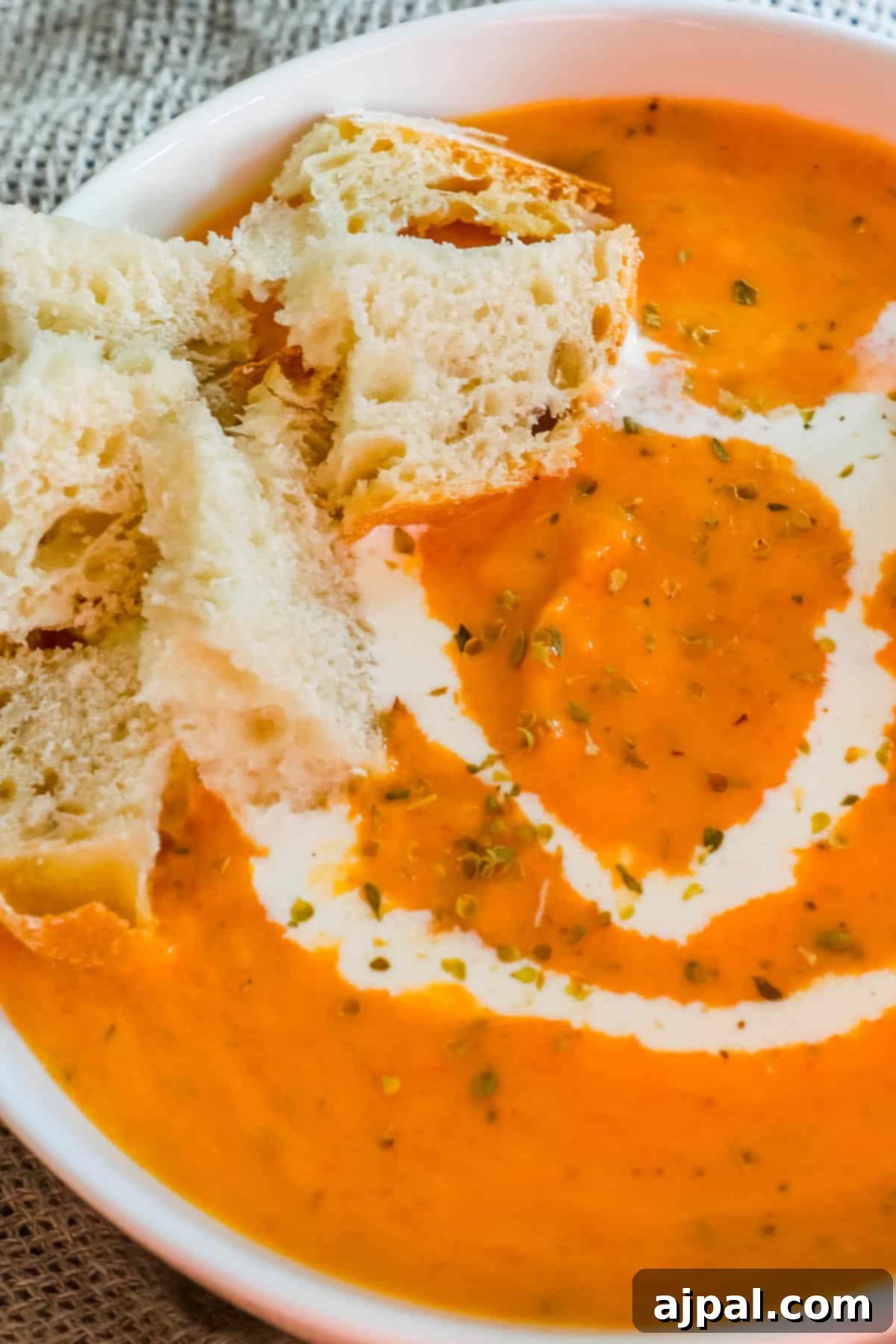 Hearty Roasted Tomato Soup 3 A close-up of a bowl of creamy roasted tomato soup, richly textured and garnished with a swirl of cream and fresh basil, ready to be enjoyed.
