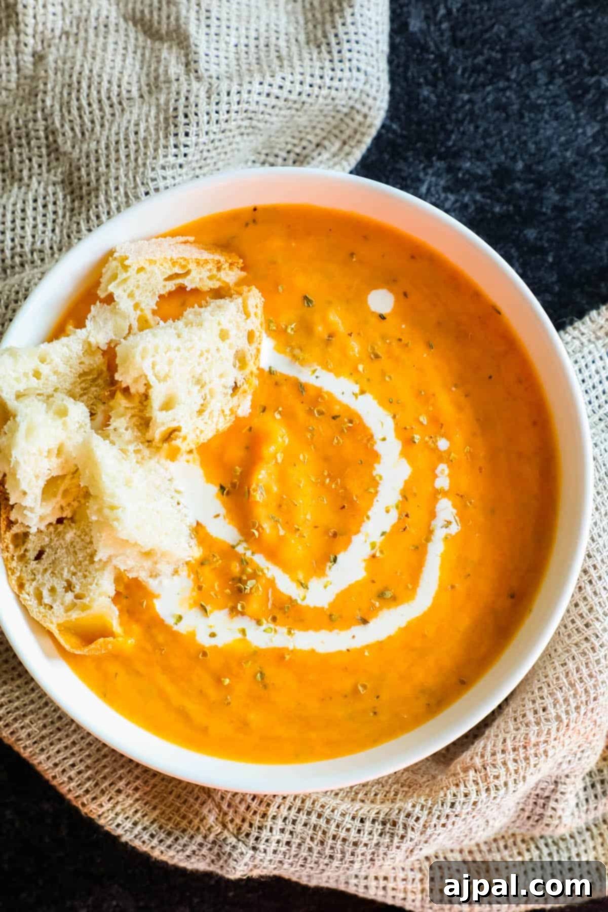 Hearty Roasted Tomato Soup 4 A bowl of vibrant orange creamy roasted tomato soup, topped with crunchy croutons and a drizzle of white cream, exuding warmth and inviting texture.