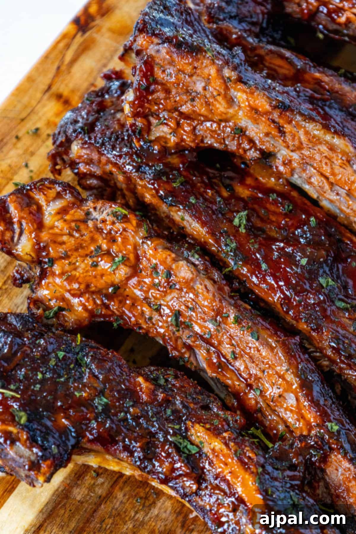 Delicious oven baked beef ribs on a rustic wooden cutting board, garnished with fresh herbs, showcasing their tender, fall-off-the-bone texture.