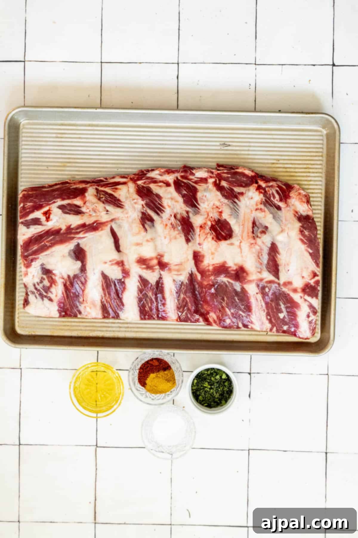 Oven baked beef ribs generously seasoned with a rich spice rub on a baking sheet, ready for slow cooking.