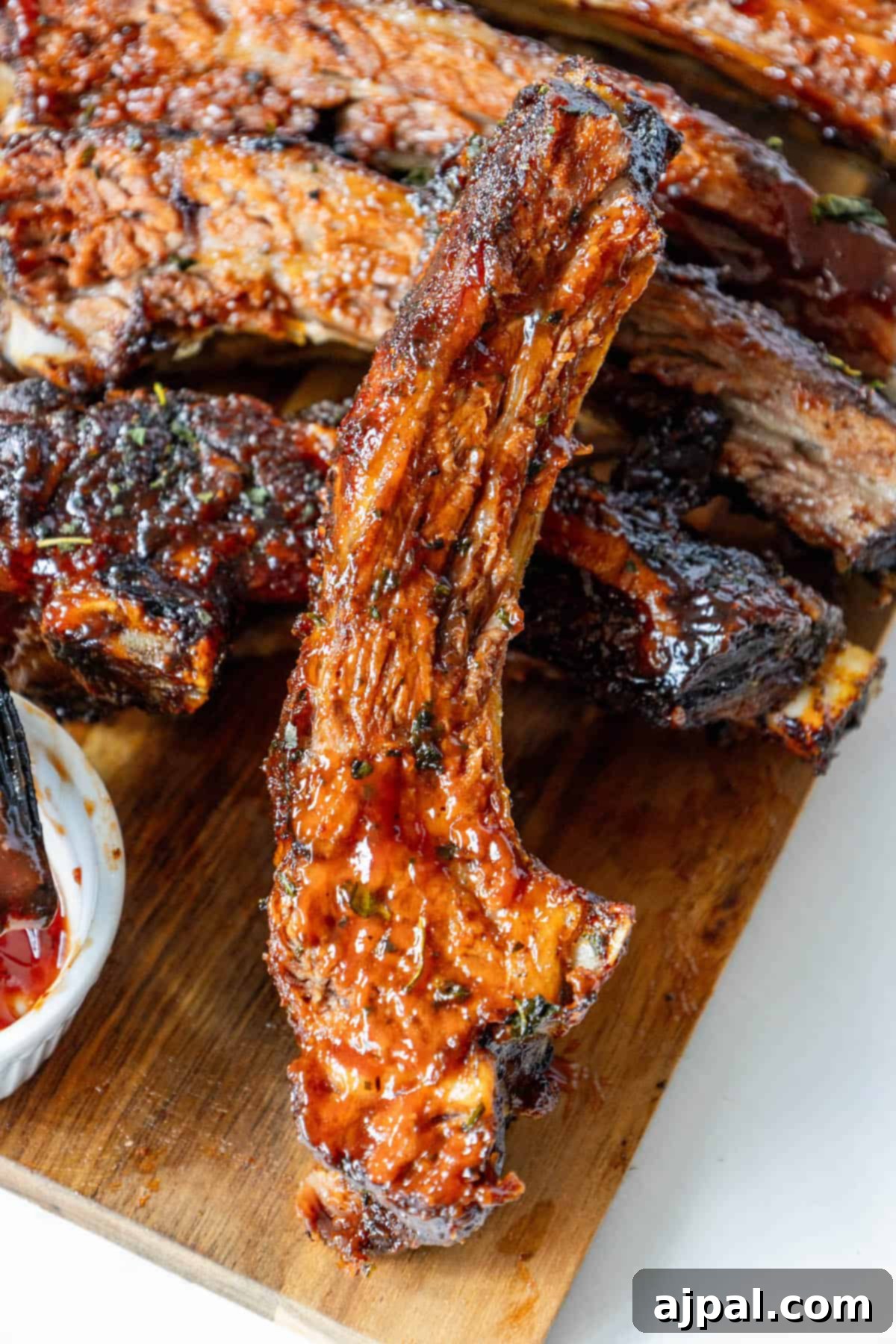 Succulent oven baked BBQ ribs, perfectly cooked and glistening with sauce, resting on a wooden cutting board, ready for carving.