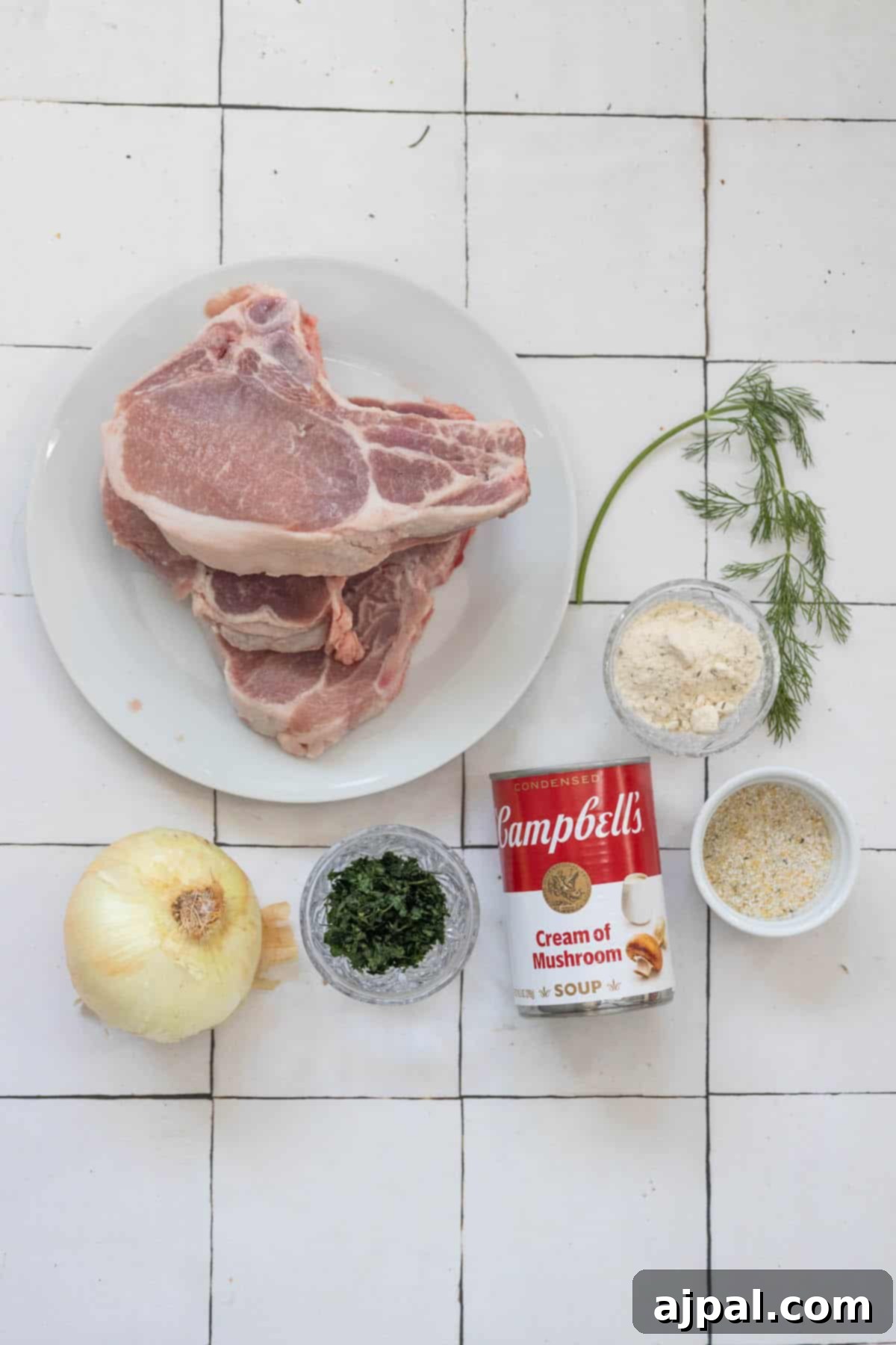 Slow Cooker Creamy Ranch Pork Chops 5 Creamy pork chops and ingredients on a white plate, showcasing fresh herbs and seasonings.