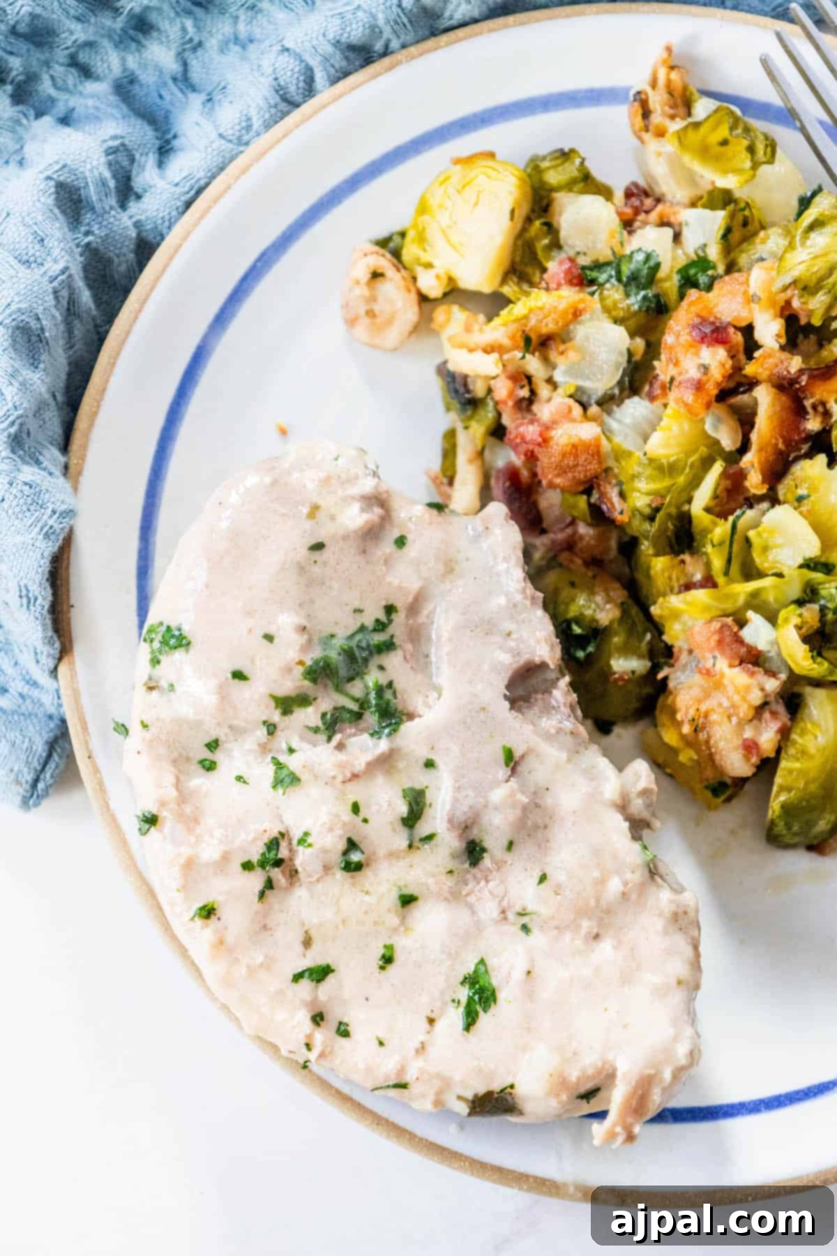 Slow Cooker Creamy Ranch Pork Chops 9 A plate of pork chops and brussels sprouts on a blue plate, slow-cooked to perfection in a Crock Pot, covered in creamy sauce.