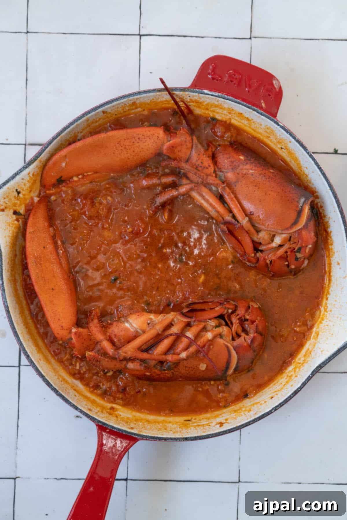 Exquisite Italian Lobster Pasta 11 Two Venetian lobsters in a red skillet on a tiled floor.