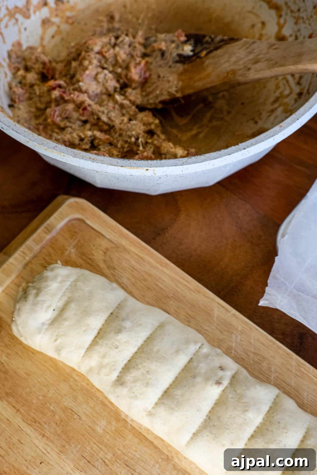 A wooden cutting board with a rolled-up crescent dough log.