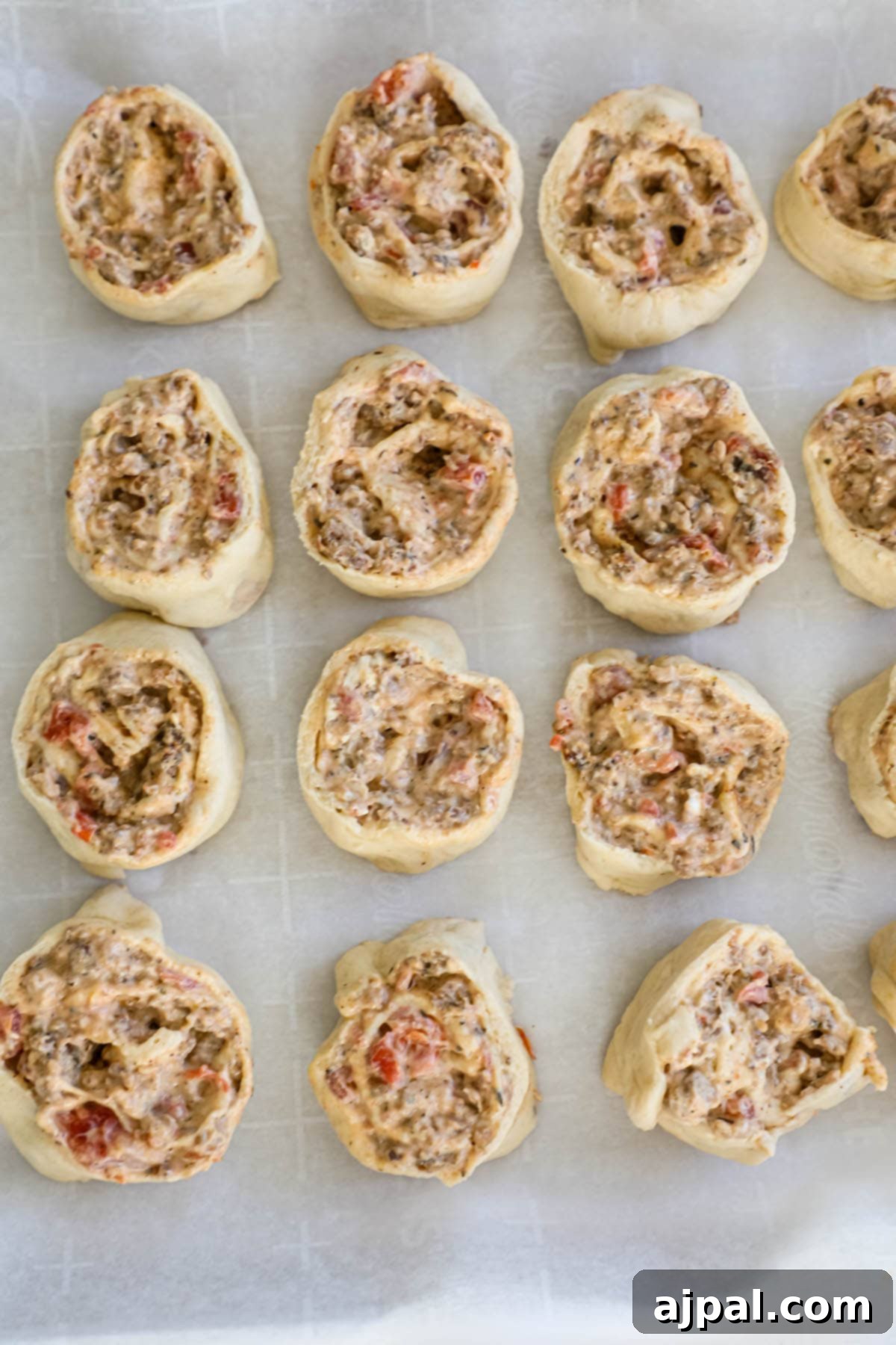 Sliced sausage pinwheels arranged on a parchment-paper lined baking sheet.