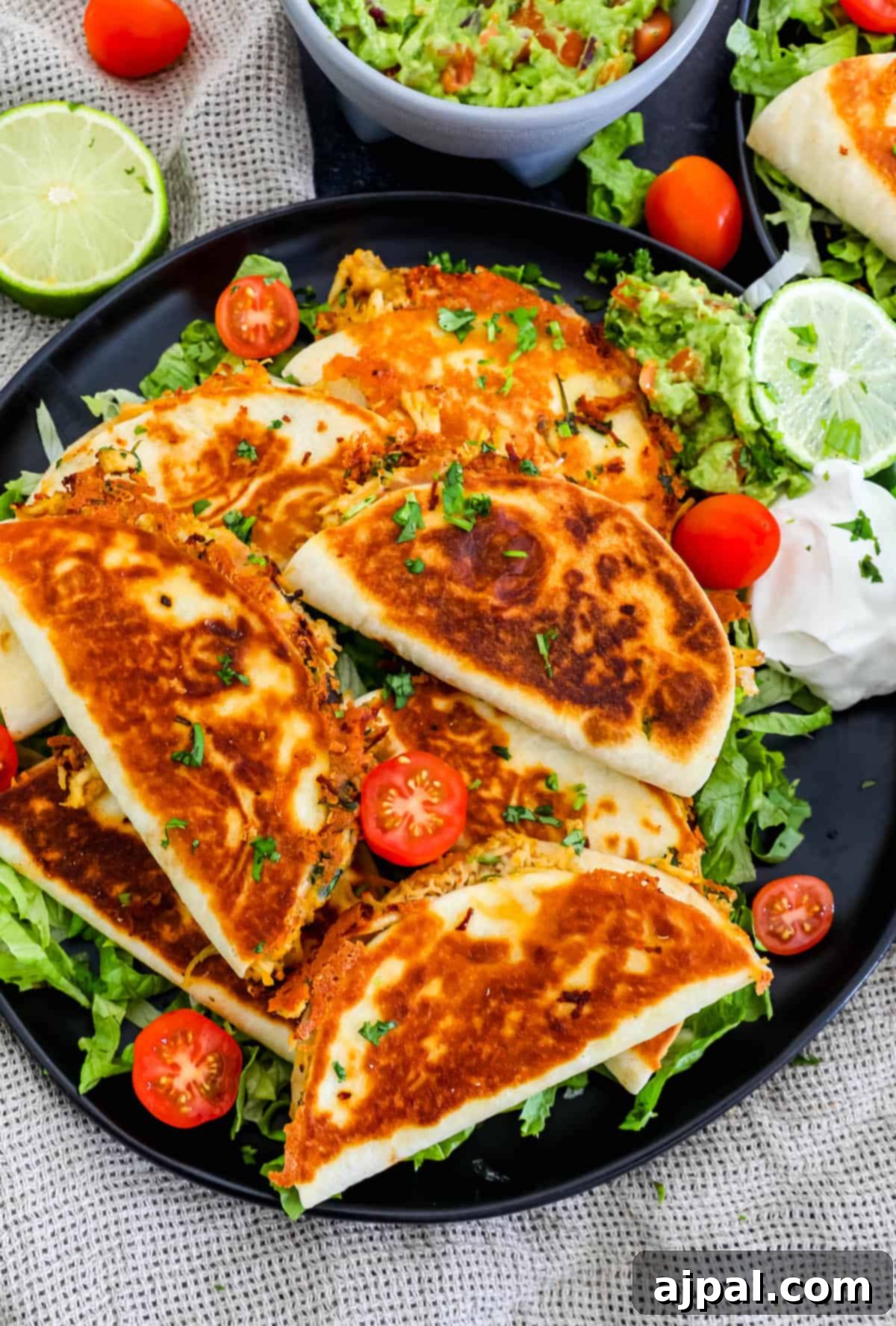 Bite-Sized Chicken Quesadillas 2 Mini chicken quesadillas on a black plate with tomatoes and guacamole.