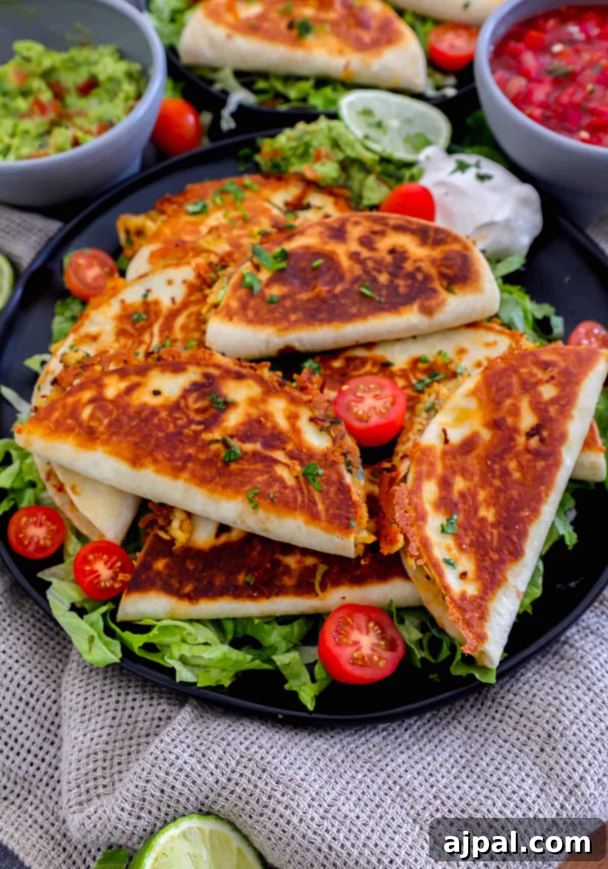 Mini chicken quesadillas on a black plate with tomatoes and guacamole.