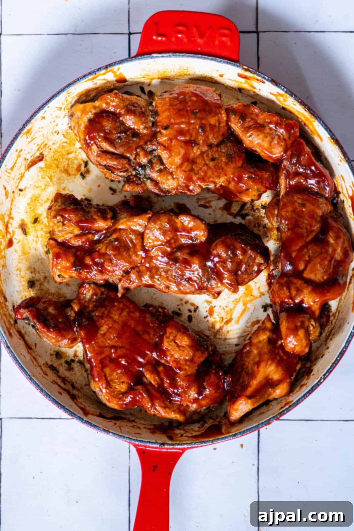 A pan with boneless BBQ country style ribs in it on a tiled floor.