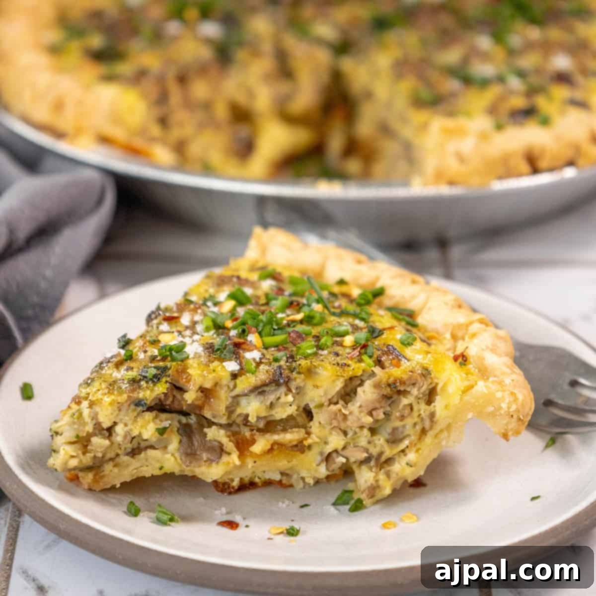 Forest Mushroom Quiche 3 A delectable slice of mushroom quiche, perfectly baked and served on a plate with a fork.