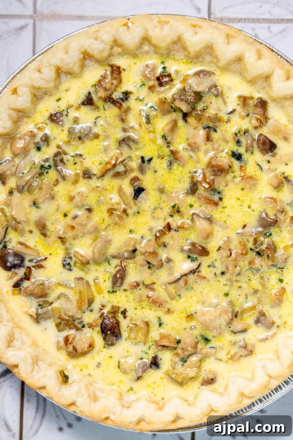 Forest Mushroom Quiche 6 A whole mushroom quiche sitting on a rustic tiled surface, highlighting its golden-brown crust.