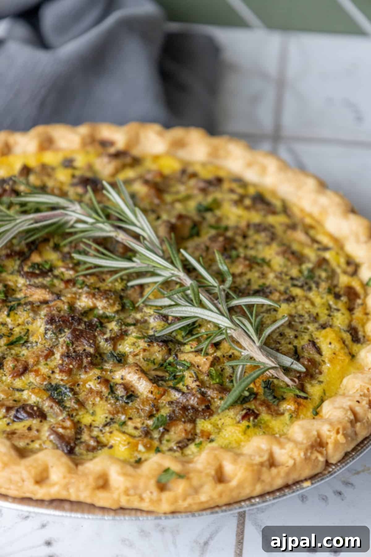 Forest Mushroom Quiche 10 A savory mushroom quiche garnished with fresh rosemary sprigs on a dark background.
