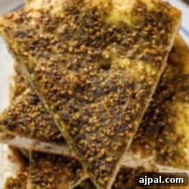 A plate with a piece of bread with sesame seeds and Za'atar on it.